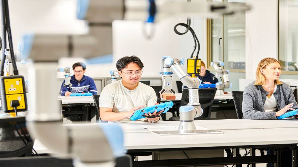 Several students controlling robot arms using tablet computers.