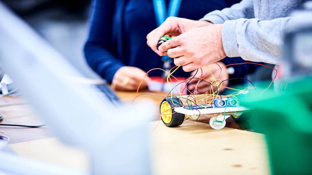 Several people working on a small wheeled robot.