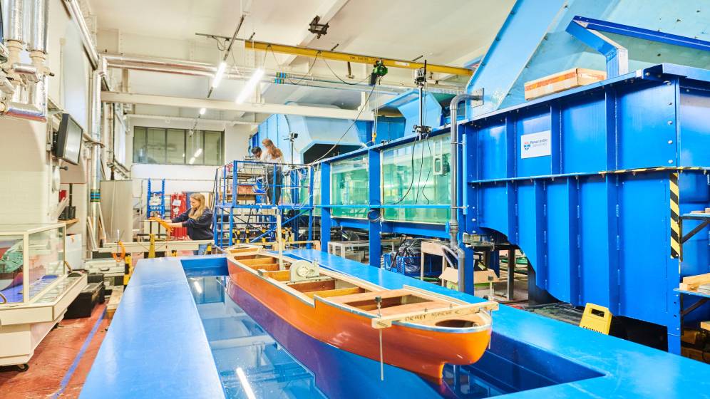 A wooden boat model floating in a marine testing tank.