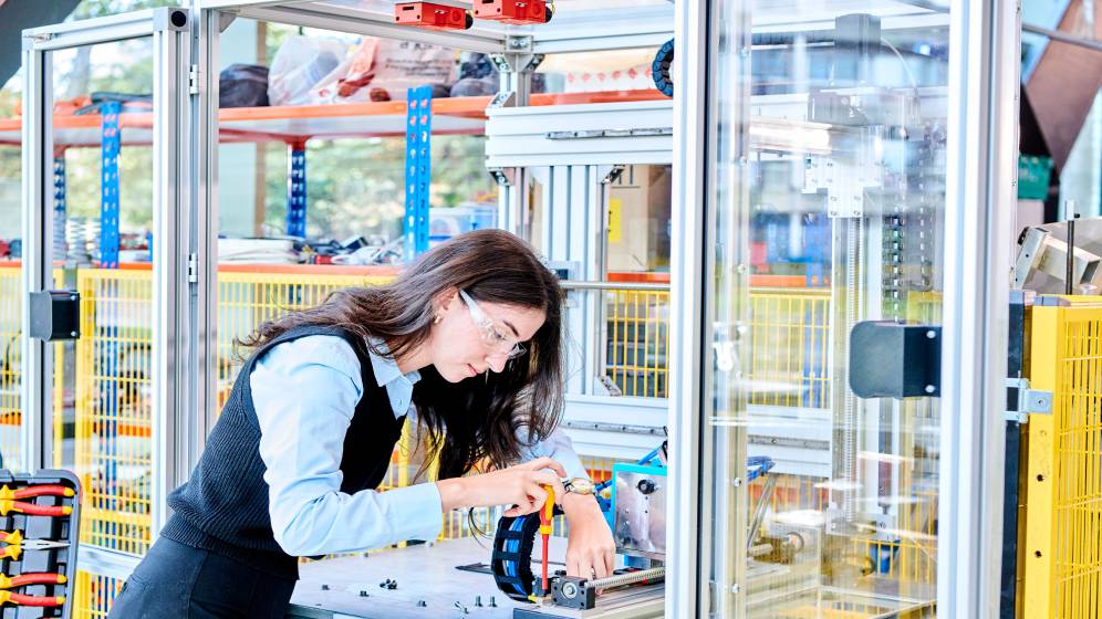 A female student using a screwdriver on a piece of equipment.