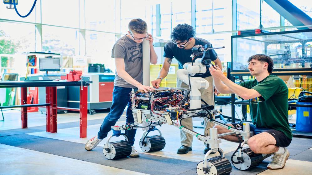 Three students working on a wheeled robot.